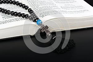 Closeup of opened Holy Bible and rosary beads with cross on black background. Religion concept. Cyrillic text