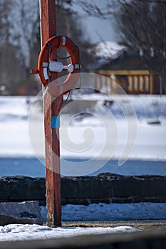 A closeup of an orange life saver ring hanging on wooden pole on the beach boulevard