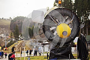 Closeup of orange snow maker machine with fan blades near ski resort slope in autumn, fall