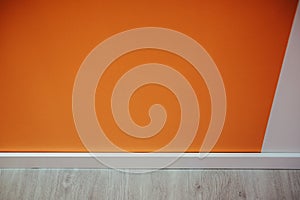 Closeup of an orange wall  and a white baseboard