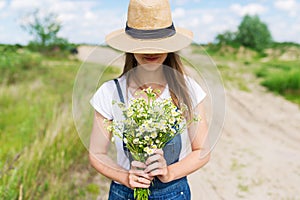 Closeup outdoor portrait of a beautiful young woman in hat. Attractive happy girl in a field with bouquet of flowers