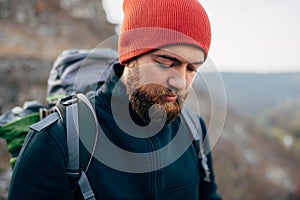 Closeup outdoors portrait of young handsome hiker male hiking in mountains wearing red hat. Traveler bearded man trekking