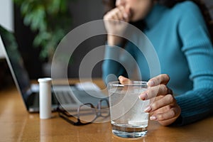 Closeup of painkiller dissolving in glass of water. Sick business woman take medical pill in office