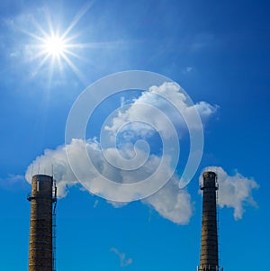 Closeup pair of industrial pipes with smoke on blue sunny sky background