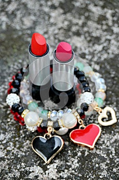 closeup the pair of red,pink color lipstick silver black tube with red white plastic beads bracelet soft focus natural grey brown