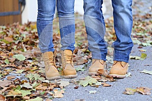 Closeup of a pair wearing the same boots and jeans and standing outdoors in autumn