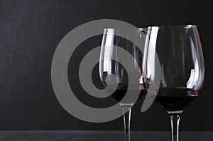 Closeup of pair of wine glasses with red wineagainst dark wall. Delicious best luxury wine