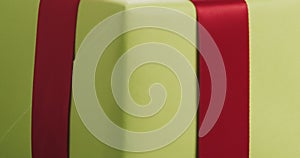 Closeup pan of green paper gift box with red ribbon bow on oak table