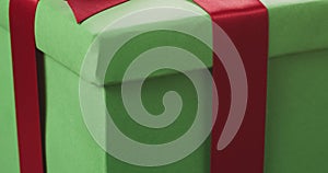Closeup pan of green paper gift box with red ribbon bow on oak table
