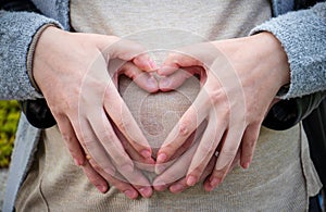 Closeup of parents forming a heart with hands on the belly of a pregnant female - parenthood concept