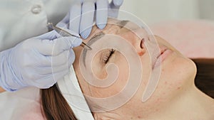 Closeup part of face, woman plucking eyebrows depilating with tweezers.