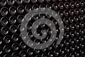 Closeup pattern from bottom of old dark dusty wine bottles in rows in cellar, basement, wine warehouse, winery. Concept