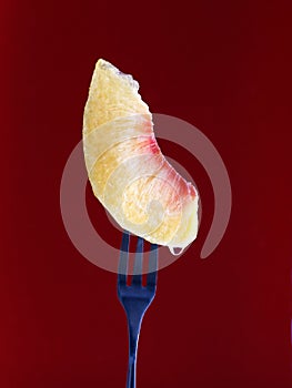 Closeup of a peach slice on a fork in a maroon background
