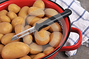 Closeup on peeler with potatoes ia colander