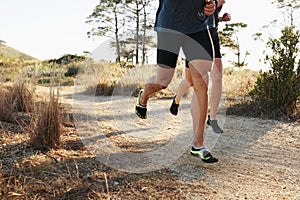 Closeup, people and legs with running for fitness, exercise or outdoor training on dirt road. Person and runner with