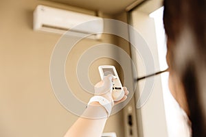 Closeup people using remote control adjust room temperature in home office pointing to Air conditioner in hot summer season