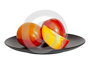 Closeup of persimmon fruit on a black plate on a white background