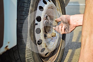 Closeup of person checking fixing bolts on vehicle tire with bare hands.