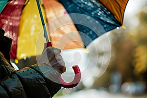 closeup of a person gripping a colorful umbrella handle on a drizzly day