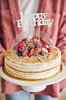 Closeup of a person holding the fruity cake with a Happy Birthday topper
