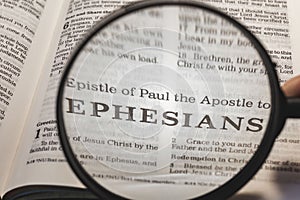 Closeup of a person holding a magnifier and reading the book of Ephesians from the New Testament