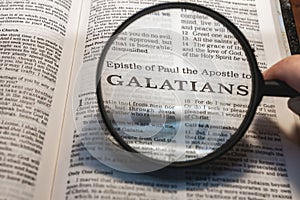 Closeup of a person holding a magnifier and reading the book of Galatians from the New Testament