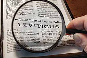 Closeup of a person holding a magnifier and reading the book of Leviticus from the New Testament