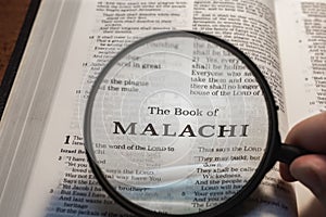 Closeup of a person holding a magnifier and reading the book of Malachi from the New Testament