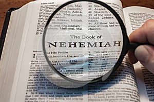 Closeup of a person holding a magnifier and reading the book of Nehemiah from the New Testament
