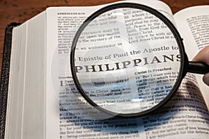 Closeup of a person holding a magnifier and reading the book of Philippians from the New Testament