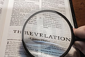 Closeup of a person holding a magnifier and reading the Revelation from the New Testament