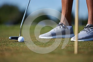 Closeup of person playing golf with golf club hitting ball on grass