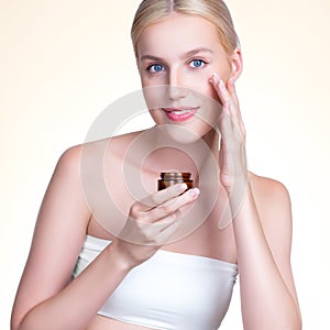 Closeup personable woman applying moisturizer cream on her face for perfect ski