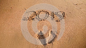 Closeup photo of 2019 New Year numbers and footrpints on wet sand at ocean beach. Concept of New Year, Christmas and