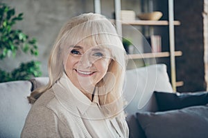 Closeup photo of amazing blond adorable aged granny homey good mood toothy beaming smiling cheerful sitting comfort sofa