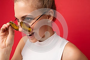 Closeup photo of attractive amusing young blonde woman wearing everyday stylish clothes and modern sunglasses isolated