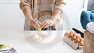 Closeup photo of baker cracking egg for dough. Woman preparing dumplings in kitchen at home