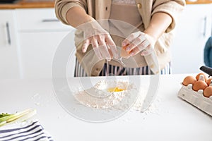 Closeup photo of baker cracking egg for dough. Woman preparing dumplings in kitchen at home