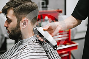 Closeup photo of a barber`s hand with a haircut, creates a stylish hairstyle for a bearded man in a hair salon for men.