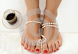 Closeup photo of beautiful female feet with red pedicure on white and decorated with pearls