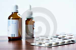 Closeup photo of blister pack with tablets, vials or drops on brown wooden table top. Blurred white background