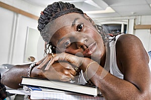 Closeup portrait of bored young African American student resting on stack of books in classroom