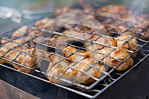 Closeup photo of chicken wings in tomato sauce, roasting in the grill rack on charcoal grill in hiking picnic. Selective focus