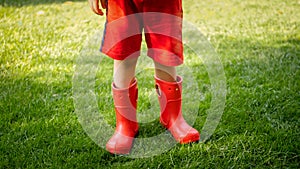 Closeup photo of child wearing red rubber boots standing on grass at park