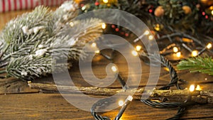 CLoseup photo of Christmas tree branches and glowing light garlands on rustic wooden background