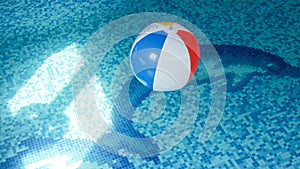 Closeup photo of colorful striped inflatable beach ball floating on the water surface at swimming pool