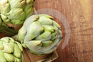 A closeup photo of a globe artichoke on a dark rustic wooden background