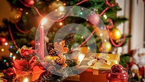 Closeup image of golden gift box and burning candle against beautiful Christmas tree