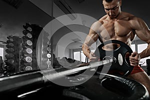 Closeup photo of handsome bodybuilder guy prepare to do exercises with barbell in a gym, keep barbell plate in hands