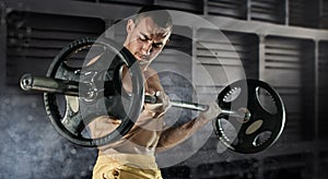 Closeup photo of handsome bodybuilder guy prepare to do exercises with barbell in a gym, keep barbell plate in hands